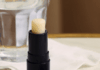 霍瑞斯选择回收包装,展现负责任的姿态 site-industries-cosmetiques 一支黑色的润唇膏,瓶盖上刻有品牌名称 "HORACE",放在大理石表面上,旁边放着一杯水和一张白色餐巾纸。.