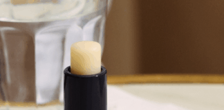site-industries-cosmetiques 一支黑色的润唇膏，瓶盖上刻有品牌名称 "HORACE"，放在大理石表面上，旁边放着一杯水和一张白色餐巾纸。.