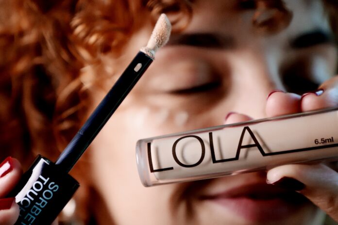 site-industries-cosmetiques Una persona con el pelo rizado sostiene un tubo de corrector con la etiqueta 