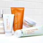 site-industries-cosmetiques Five skincare products by Kate Somerville, from creams to exfoliators, are presented on a white checkered background. This Rare Beauty Brands collection features white and orange packaging, clearly labeled with Unilever's trusted name.