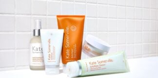 site-industries-cosmetiques Cinq produits de soin de la peau de Kate Somerville, de la crème à l'exfoliant, sont présentés sur un fond de carreaux blancs. Cette collection Rare Beauty Brands présente des emballages blancs et orange, clairement étiquetés avec le nom de confiance d'Unilever.