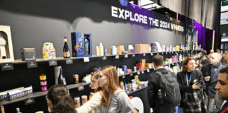 site-industries-cosmetiques 一群人正在观看一面展示墙，墙上挂着 "探索 2024 年的赢家 "的牌子，上面展示着各种产品包装。.