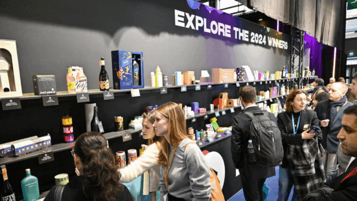 site-industries-cosmetiques Um grupo de pessoas olha para uma parede de exposição que mostra vários produtos embalados sob um letreiro que diz 