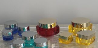 site-industries-cosmetics 蓝色、红色和黄色的各种塑料化妆品罐和容器，配以银色盖子，摆放在质感透明的表面上，背景为纯灰色。.