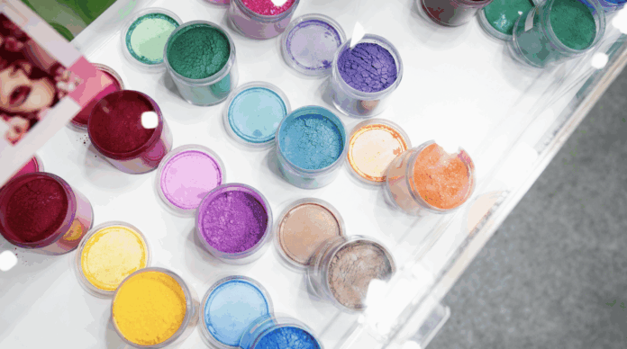 site-industries-cosmetiques Vários frascos transparentes cheios de pigmentos coloridos em pó estão dispostos numa superfície branca, apresentando tonalidades vibrantes que realçam as inovações em biotecnologia. Parte de um cartão fotográfico a cores é visível, evocando o espírito da in-cosmetics Asia 2025.