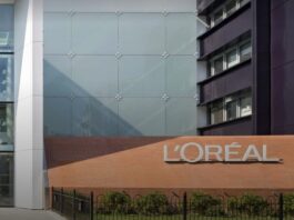 site-industries-cosmetiques 一座现代建筑的外观，砖墙上固定着一个巨大的 "欧莱雅 "标志，旁边是玻璃幕墙和绿地，体现了品牌的成长和创新。.
