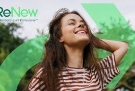 site-industries-cosmetiques 一位身着条纹衬衫、留着棕色长发的女士微笑着站在外面，闭着眼睛。左上角的绿色图案上印有 "ReNew by Kimberly-Clark Professional "字样。