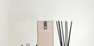 site-industries-cosmetiques 四个带插图标签的香水扩香瓶、一个扩香盒和一个小喷雾瓶摆放在浅色木质表面上，背景柔和而模糊。.