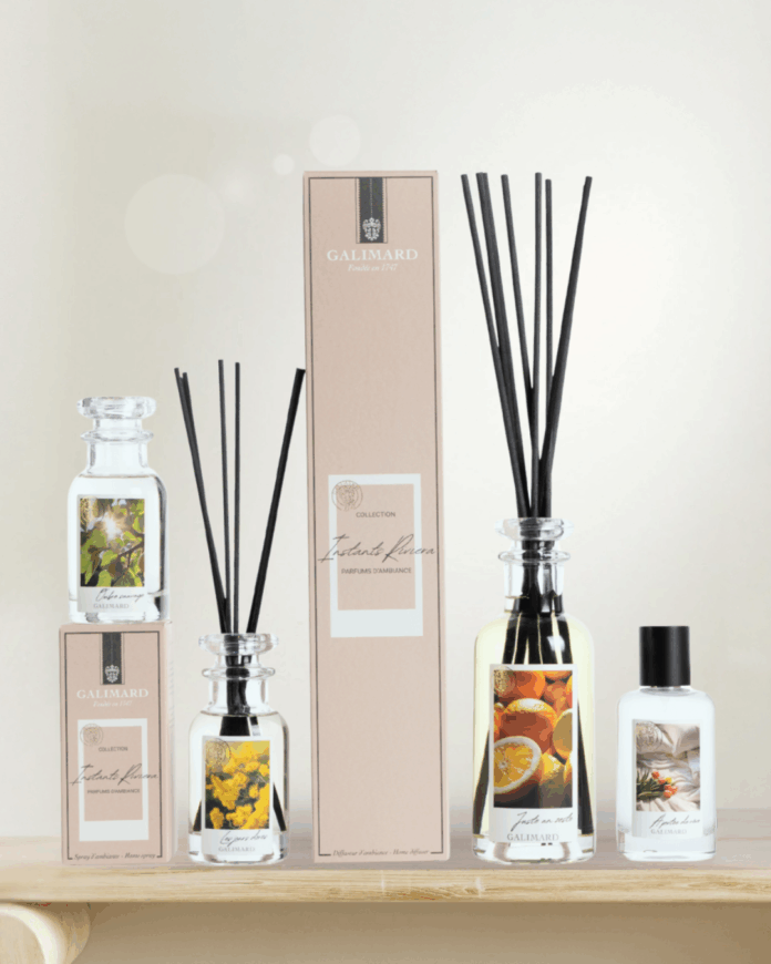 site-industries-cosmetiques 四个带插图标签的香水扩香瓶、一个扩香盒和一个小喷雾瓶摆放在浅色木质表面上，背景柔和而模糊。.