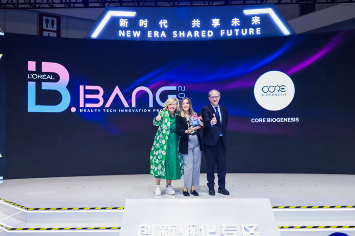 site-industries-cosmetiques 三个人站在舞台上，对着显示欧莱雅 B.BANG 2024 和 Core Biogenesis 徽标的大屏幕竖起大拇指，大屏幕上显示着 "欧莱雅 B.BANG 2024 "和 "Core Biogenesis"。 