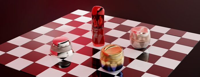 site-industries-cosmetiques Four containers of Shiseido skincare products, including jars and a large bottle, are arranged on a red and white checkerboard surface under dramatic lighting, reflecting Shiseido's medium-term 2030 strategy for beauty innovation.