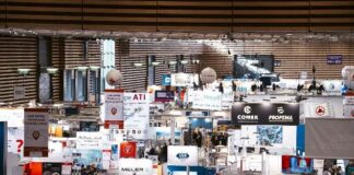 site-industries-cosmetiques 大型室内贸易展，有许多展台、横幅和展品。许多人在展台间徘徊和交流。在这个热闹的场景中，印有公司名称和标识的标志清晰可见。.