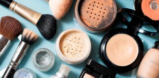 site-industries-cosmetiques 浅蓝色的表面上陈列着各种化妆产品和化妆刷。产品包括散粉和粉饼、粉底液、荧光笔、眼影盒和几支化妆刷。.