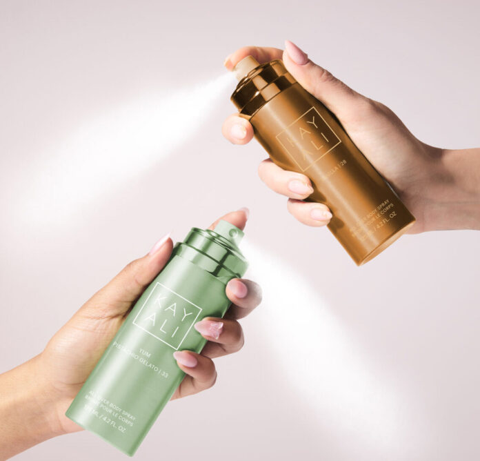 site-industries-cosmetiques Dos manos sostienen y rocían dos botellas de bruma AYALI, una verde y otra bronce, cada una de las cuales emite un chorro visible sobre un fondo claro y neutro.