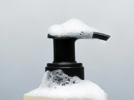 site-industries-cosmetiques 灰色背景上有一个带泵盖的 Gris Charnel 沐浴露瓶，瓶身部分覆盖着泡沫肥皂泡。瓶身标签显示容量为 300 毫升或 10.1 盎司。.