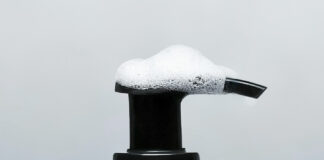 site-industries-cosmetiques 灰色背景上有一个带泵盖的 Gris Charnel 沐浴露瓶，瓶身部分覆盖着泡沫肥皂泡。瓶身标签显示容量为 300 毫升或 10.1 盎司。.