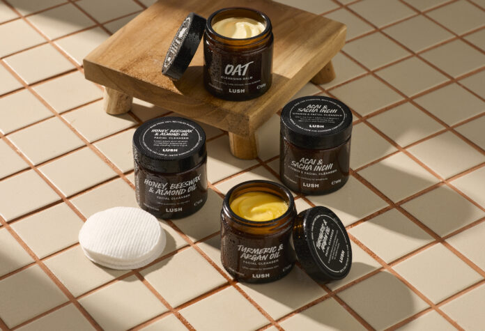 site-industries-cosmetiques 四罐打开的 Lush 面霜摆放在瓷砖地面上，旁边还有两块化妆棉和一个小木台。每个罐子上都标有成分，如燕麦片、姜黄、摩洛哥坚果油和杏仁油。.