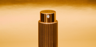 site-industries-cosmetiques Un flacon pulvérisateur cylindrique doré, à la texture nervurée, se tient debout sur un fond doré réfléchissant.