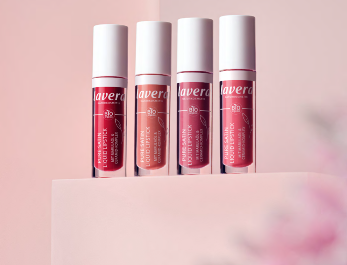 site-industries-cosmetiques Quatre tubes de rouge à lèvres liquide Lavera Pure Satin de différentes teintes se tiennent debout sur une surface rose clair sur un fond rose. Les rouges à lèvres sont disposés en rangée, les étiquettes tournées vers l'avant.