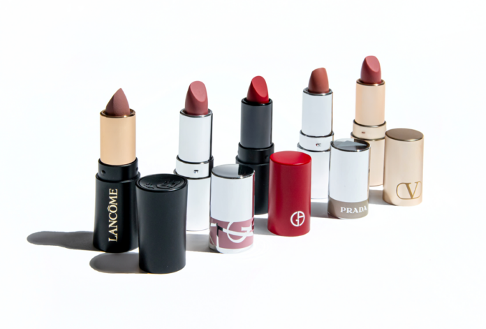 site-industries-cosmetiques Seis barras de labios de diferentes marcas de lujo, cada una sin tapón y colocada junto al tubo. Las marcas visibles son Lancôme, Chanel, Hermès, Giorgio Armani, Prada y Valentino, de izquierda a derecha.