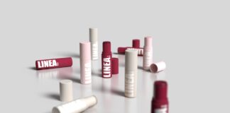 site-industries-cosmetiques 几支标有 "LINEA "字样的红白相间的圆柱形润唇膏管散落在光滑的反光表面上，有些盖子还在，有些则被取下，背景是纯灰色。.