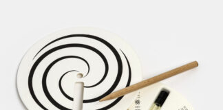 site-industries-cosmetiques Une boîte d'emballage circulaire avec un couvercle amovible présentant un motif en spirale noir et une ouverture. À l'intérieur se trouvent six petites fioles en verre contenant des liquides de différentes couleurs et un outil en bois, disposés autour d'un moyeu central - idéal pour les accessoires. PCD 2026.