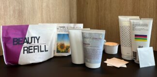 site-industries-cosmetiques 在木质底座上的深色表面上摆放着一组美容产品容器，包括管状、罐状、蜡烛状、折叠包和标有 "BEAUTY REFILL "的补充装袋。.