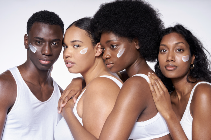 site-industries-cosmetiques 四个人并排站着，每个人的脸颊上都有一条白霜。他们身穿白色上衣，表情中性，面对镜头，背景淡雅素净。.