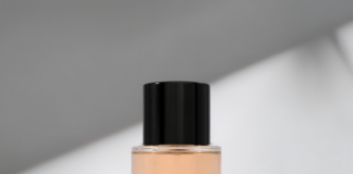 site-industries-cosmetiques 一个透明的玻璃瓶，里面装满了透明的桃红色液体，瓶口有一个闪亮的黑色瓶盖，放置在一个有光影角度的白色表面上。.