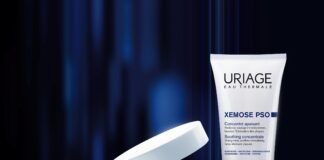 site-industries-cosmetiques 在深蓝色的抽象背景上描绘了三种 Uriage 护肤产品：滴管瓶、开盖瓶和尖头挤压管。所有容器上都贴有蓝白相间的标签。.