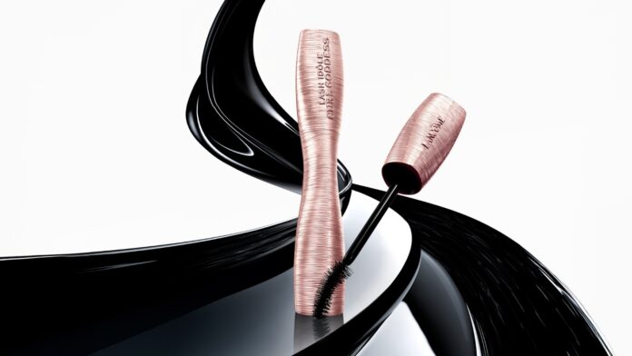 site-industries-cosmetiques Un tubo de máscara de pestañas rosa metalizado y una varita a juego con cerdas negras se presentan en vertical, rodeados de suaves y brillantes remolinos negros sobre fondo blanco.