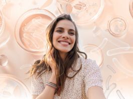 site-industries-cosmetiques Uma jovem mulher com longos cabelos castanhos sorri sobre um fundo de placas de Petri e formas científicas abstractas, reflectindo a filosofia da Nutricosmetics de brilhar a partir do interior em tons suaves de pêssego e bege.