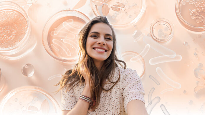 site-industries-cosmetiques Uma jovem mulher com longos cabelos castanhos sorri sobre um fundo de placas de Petri e formas científicas abstractas, reflectindo a filosofia da Nutricosmetics de brilhar a partir do interior em tons suaves de pêssego e bege.