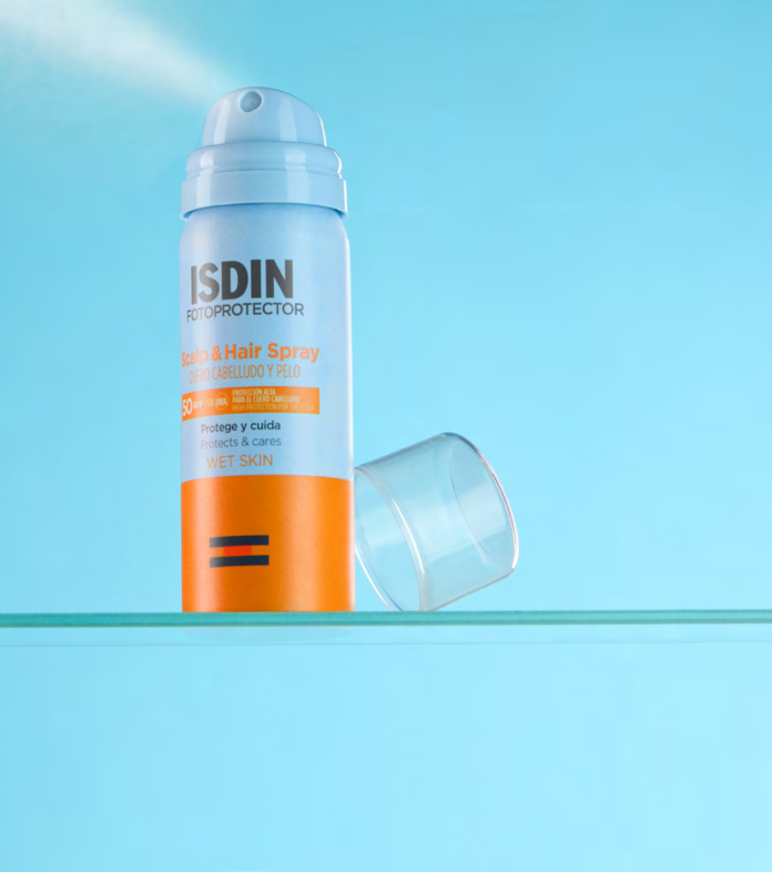 site-industries-cosmetiques 蓝色背景的玻璃架上摆放着一瓶 ISDIN FotoProtector 头皮和头发防晒喷雾 SPF 30，旁边是透明的塑料盖。.