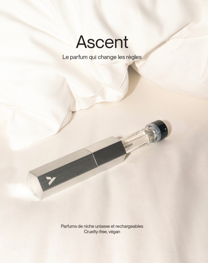 site-industries-cosmetiques Un frasco de perfume transparente con tapón y etiqueta oscuros descansa sobre una suave tela blanca. Encima se lee 