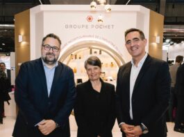 site-industries-cosmetiques Trois personnes en tenue de travail se tiennent devant un stand du Groupe Pochet lors d'un événement en intérieur. Le stand présente divers produits et comporte un motif circulaire éclairé en arrière-plan.