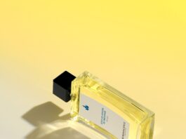 site-industries-cosmetiques 一个带黑色瓶盖的长方形玻璃香水瓶放在黄白渐变的表面上。瓶内装有黄色液体，并贴有带文字的白色标签。瓶子投下了阴影。.