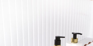 site-industries-cosmetiques 在一条白色和玫瑰金色相间的传送带上，摆放着五瓶白色化妆品，上面有不同的金色和黑色泵或喷雾器，每个瓶子上都有产品名称，如 "ALL OVER SPRAY"、"PAV"、"EuroFlow "和 "HiFlow"。.