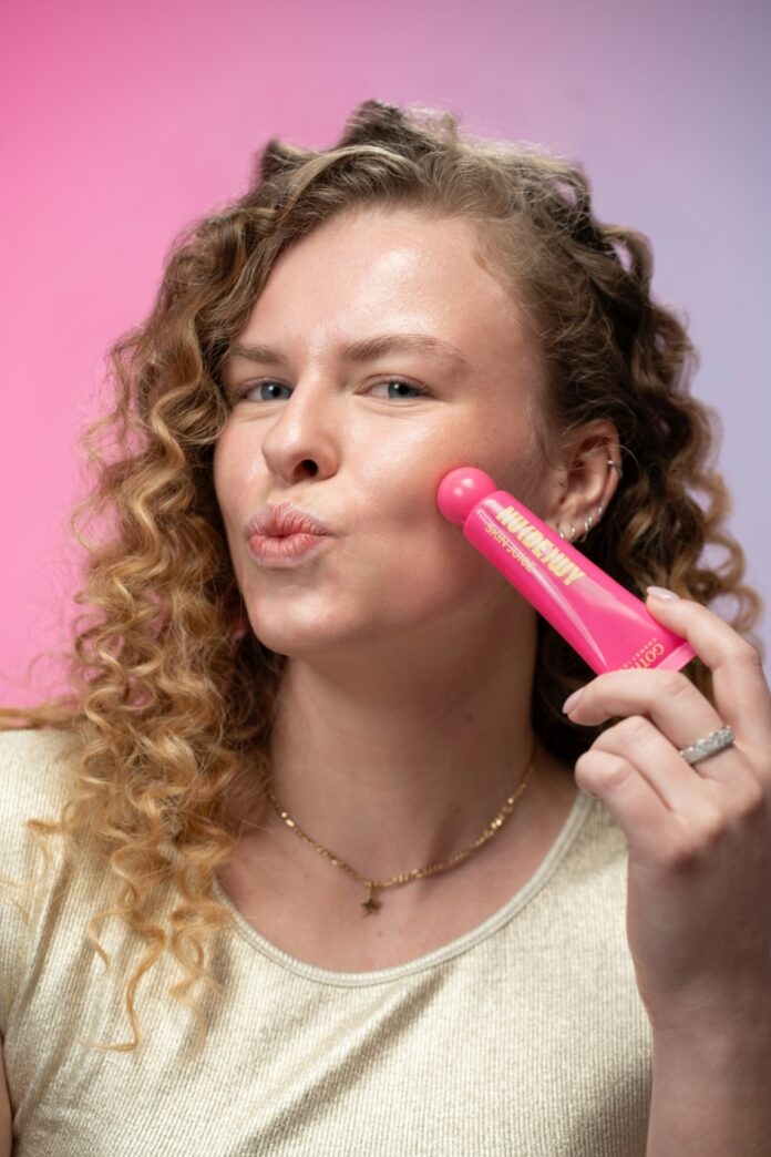 site-industries-cosmetics Uma mulher com cabelo encaracolado aperta uma ferramenta de beleza cor-de-rosa com a etiqueta 