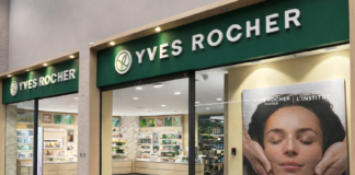 site-industries-cosmetiques 这是一家伊夫-罗歇（Yves Rocher）专卖店，绿色招牌，橱窗很大，海报上有一位女士正在接受面部护理。店内的货架上摆放着各种美容护肤产品。.