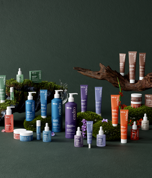 060369e9-64a7-4a5f-b52c-a53208b048b7 site-industries-cosmetiques Uma variedade de produtos para a pele em embalagens coloridas está disposta em superfícies cobertas de musgo com pequenas flores e um pedaço de madeira à deriva num fundo verde escuro.