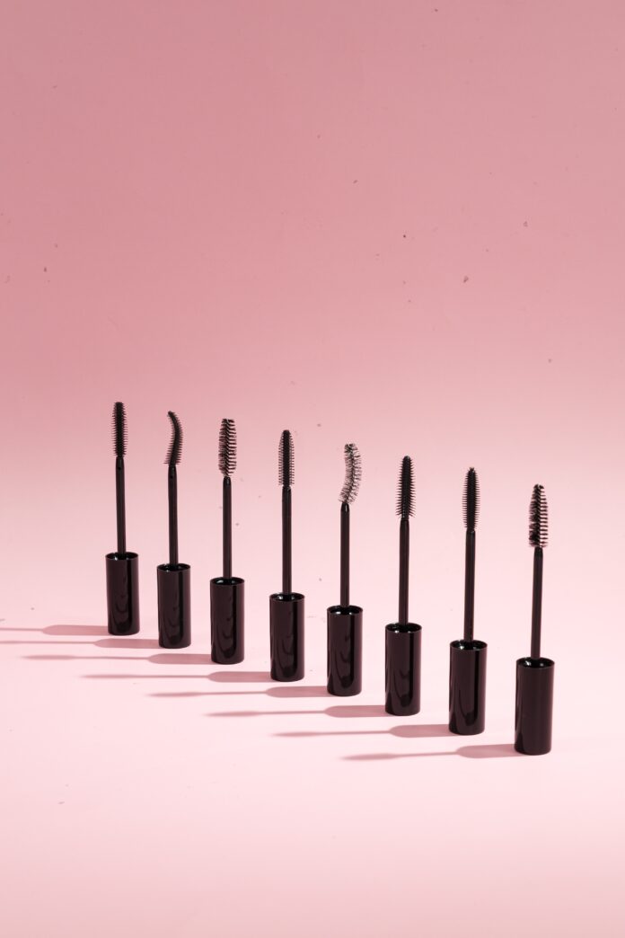 site-industries-cosmetiques Sete bastões de rímel pretos com escovas de formas diferentes estão enfileirados num fundo cor-de-rosa, cada um lançando uma sombra para a esquerda.