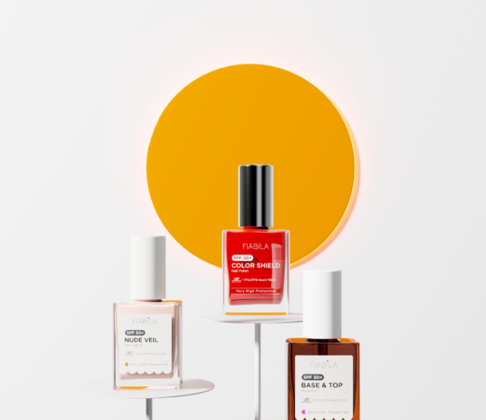 site-industries-cosmetiques Trois flacons de vernis à ongles Fiabila sont présentés sur des socles blancs devant un grand cercle orange, illustrant ainsi les innovations majeures en matière d’emballage minimaliste. Ces flacons — « Nude Veil », « Color Shield » et « Base & Top » — laissent entrevoir les tendances du salon Cosmoprof 2026.