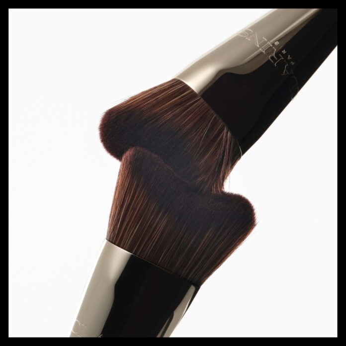 site-industries-cosmetiques Dois pincéis de maquilhagem com cerdas castanhas escuras e cabos de metal são colocados frente a frente, em ângulo, com as cerdas quase a tocarem-se, sobre um fundo branco liso.