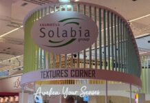 site-industries-cosmetiques Un stand d'exposition arrondi du groupe Solabia affiche des panneaux "TEXTURES CORNER" et "Awaken Your Senses". Des plantes vertes sont disposées à l'intérieur et des lattes verticales de couleur pastel forment la structure du stand.