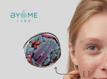site-industries-cosmetiques 一名妇女触摸脸颊的特写，放大后显示皮肤上的彩色细菌。左上角是 Byome Labs 的徽标。.
