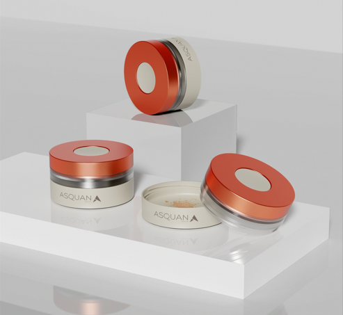 site-industries-cosmetiques 白色展示架上摆放着三个圆形化妆品容器，容器盖为金属橙色，侧面透明。其中一个打开，露出里面的散粉。包装上的品牌名称 "ASQUAN "清晰可见。.