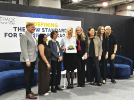 site-industries-cosmetiques A group of eight people stand on a stage, some smiling and holding a prize. Behind them, a sign reads: "Redefining the new standard in high-end packaging". Blue sofas are visible on either side.