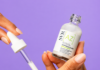 site-industries-cosmetiques 一个人手持玻璃滴管，从标有 "SVR [A] Ampoule Flash "的透明瓶子中注入白色血清，背景为纯紫色。.