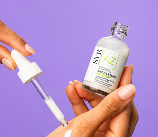 site-industries-cosmetiques 一个人手持玻璃滴管，从标有 "SVR [A] Ampoule Flash "的透明瓶子中注入白色血清，背景为纯紫色。.